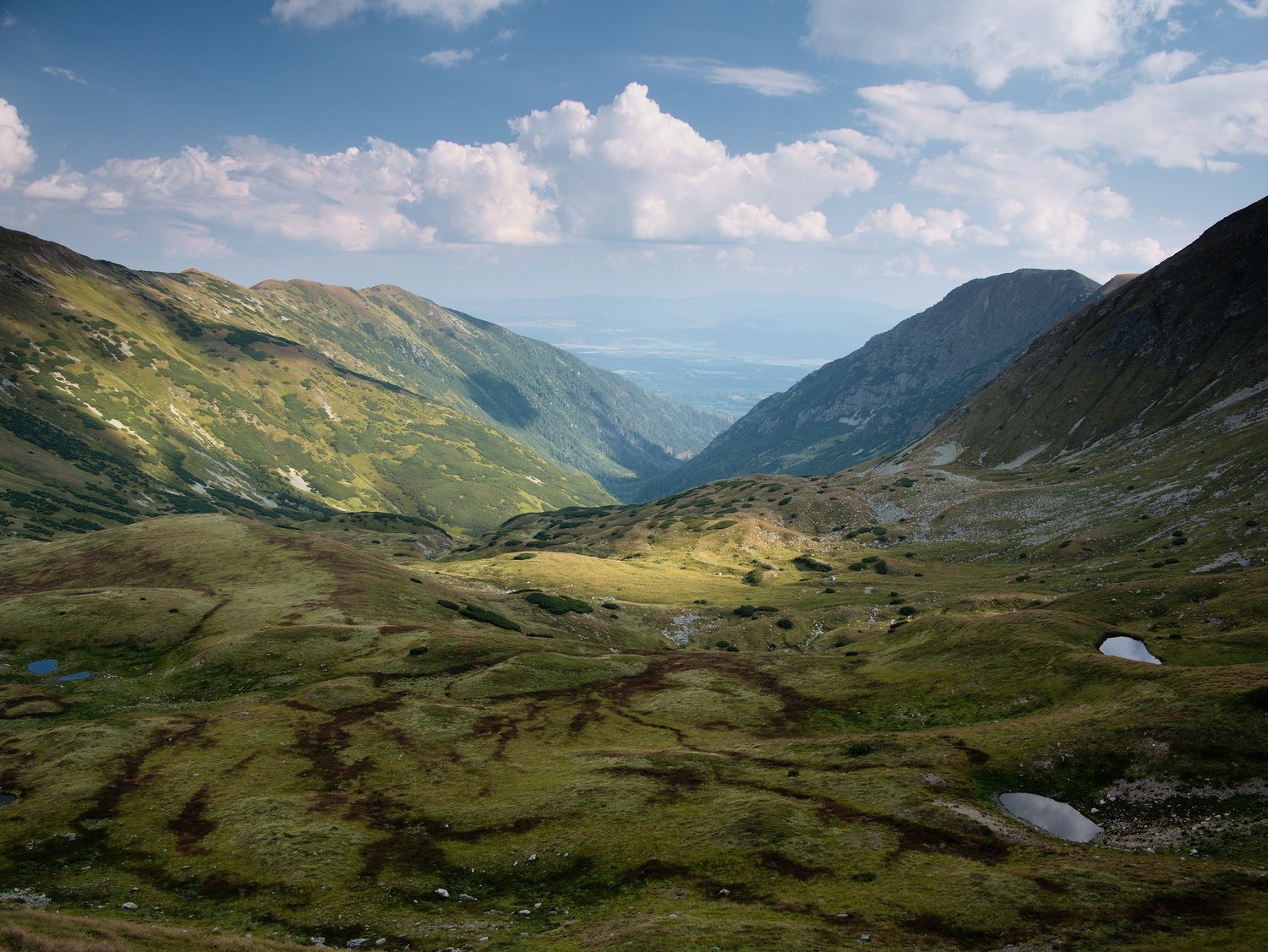 A rural landscape photo of Slovakia's green mountains with blue skies and white clouds above